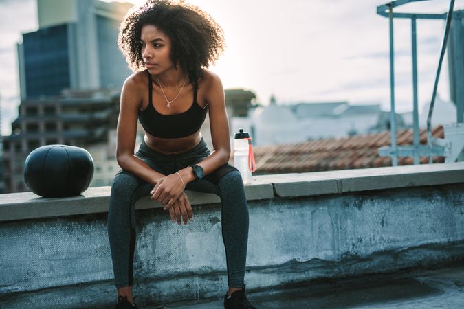 Black fit woman sitting on rooftop with medicine ball
