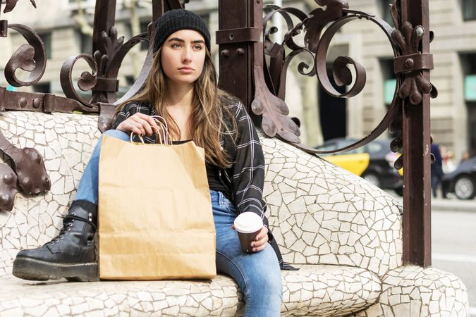 Woman in winter hat sitting outdoors holding a take away coffee after shopping