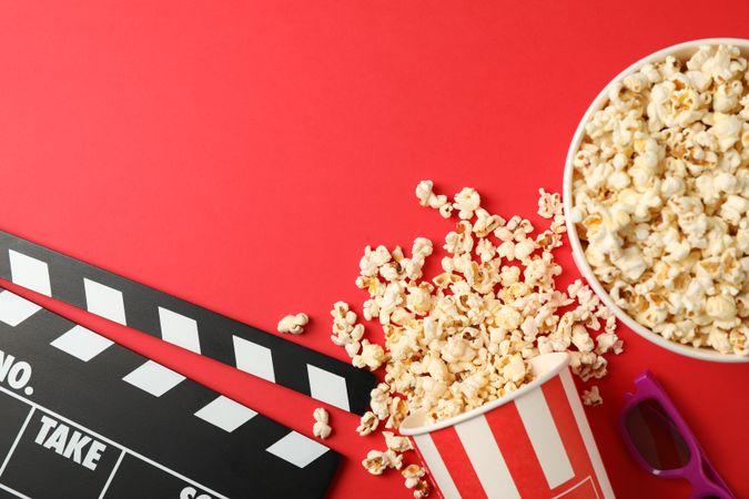Flat lay. Buckets with popcorn, 3d glasses and clapperboard on red background