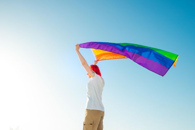 Woman holding rainbow flag under blue sky