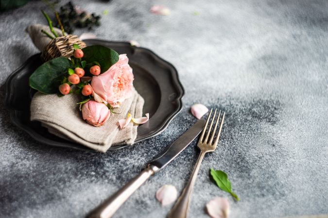 Delicate pink flowers on grey napkin and plate with silverware and place for text