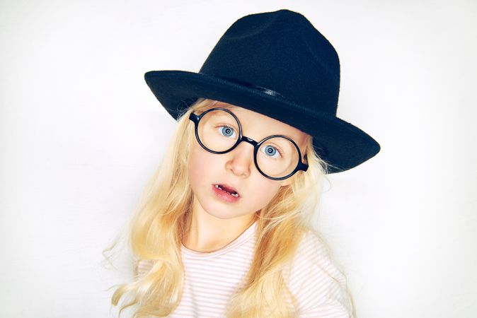 Unsmiling blonde girl wearing hat and glasses with head tilted