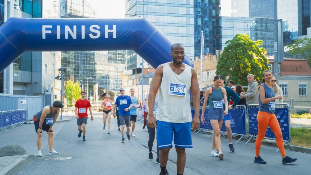Diverse Group of People Crossing the Finish Line in a City Marathon During the Day.
