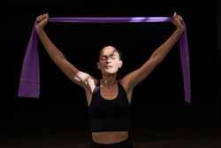 Sportswoman exercising with elastic band in dark room