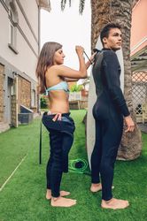 Surfer woman helping man close zipper on his wetsuit