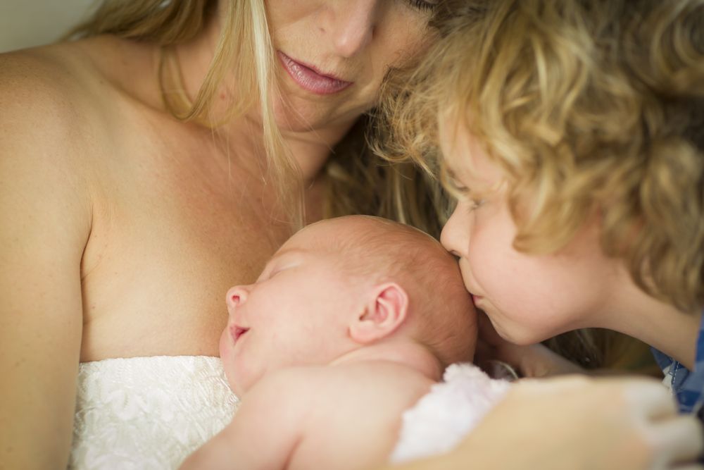Woman Holds Newborn Baby Girl as Brother Kisses Her