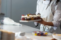 Crop baker with sweet cupcakes in kitchen