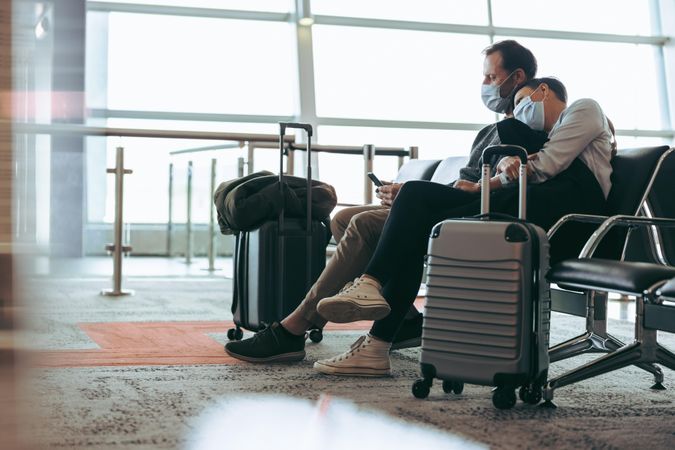 Couple wearing face masks sitting at airport terminal and waiting for the flight