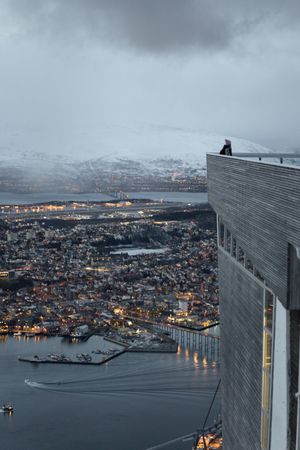 Tourists enjoying wonderful view of city against snowy mountain standing on viewpoint in evening