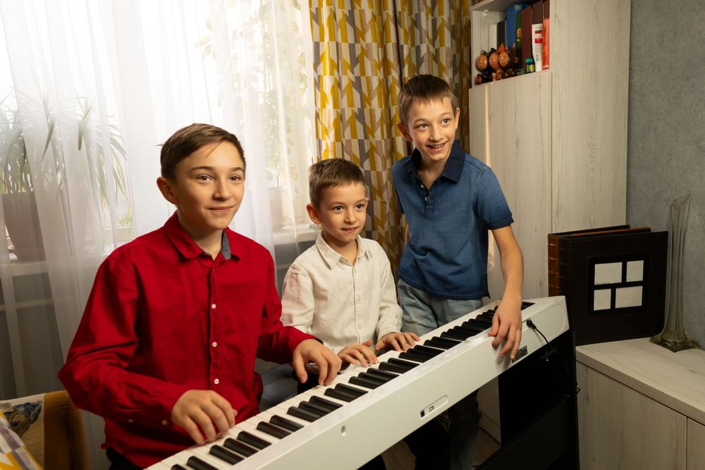 Three boys gathered around piano, enjoying music together