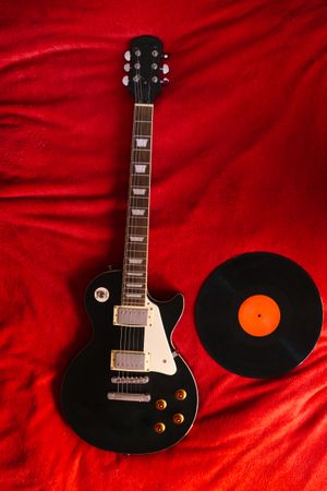 Vinyl record and electric guitar on bed