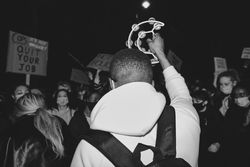 London, England, United Kingdom - March 16, 2021: Rear shot of man holding up tambourine at protest