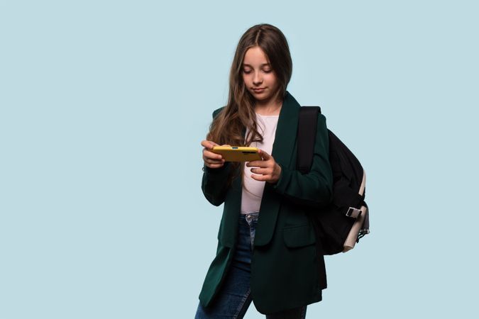 Teen girl using phone, wearing backpack, focused expression.