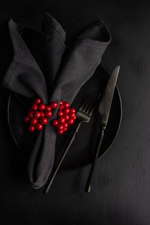 Christmas table setting with dark cutlery, plate and table with red berries