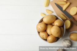 Top view of bowl full of potatoes on kitchen counter with garlic and knife, copy space 0vNdR0