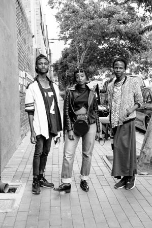 Three fashionable friends pose on sidewalk in Maboneng