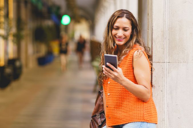 Latin woman leaning on a facade waiting and using mobile