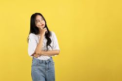 Young Asian Indonesian Woman Wearing Shirt Making Gesture Thinking about Something, Index Finger on Her Cheek.