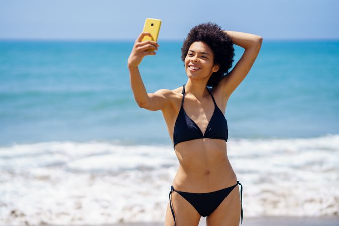 Happy woman in biking standing near the ocean taking a selfie on vacation