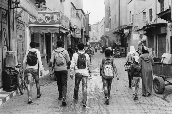 Back view of teenage boys with backpacks walking in an alley