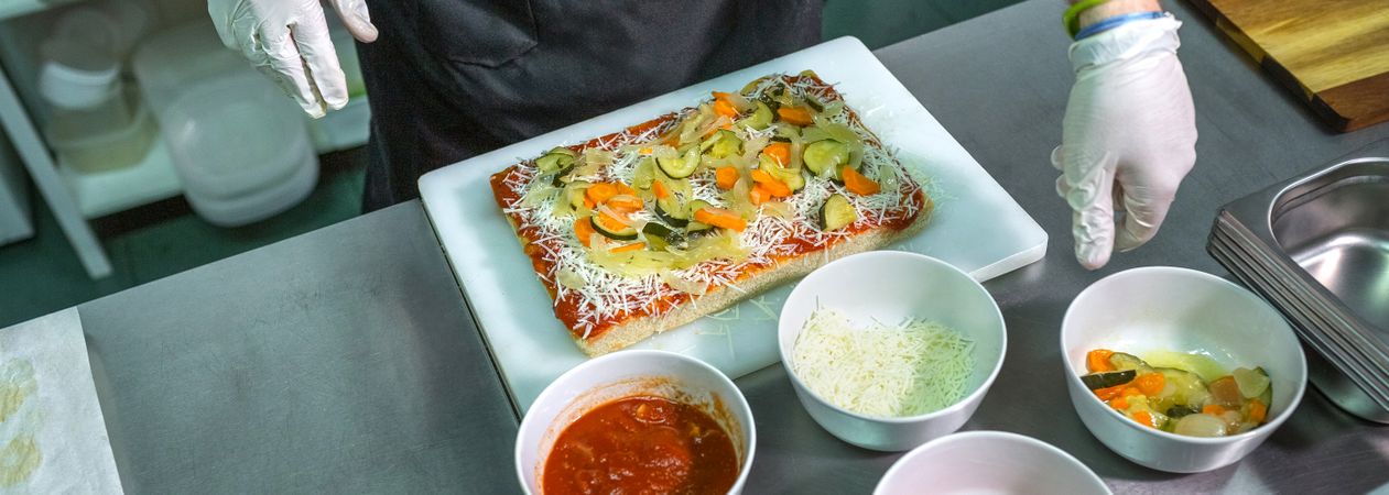 Banner of anonymous chef preparing vegetarian pizza with healthy ingredients in restaurant kitchen