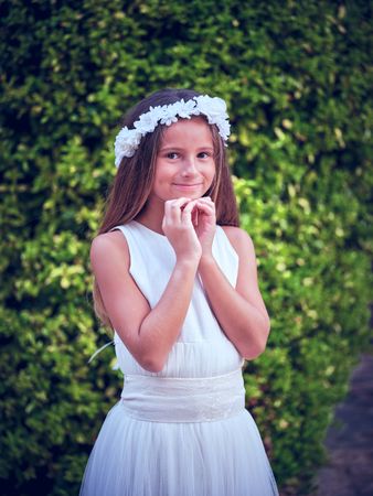 Smiling girl in flower wreath standing against green trees