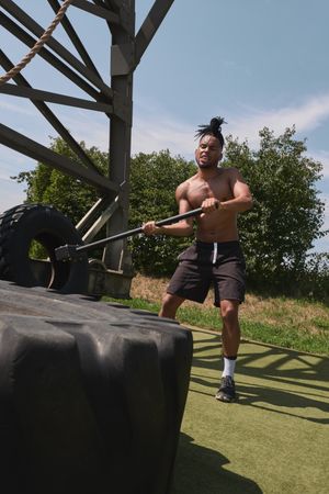 Muscular Black guy hammering tire in outdoor gym