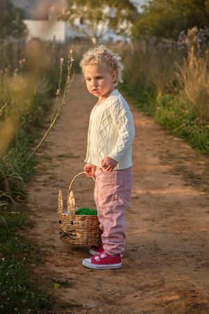Cute girl with wicker basket standing on dirt road