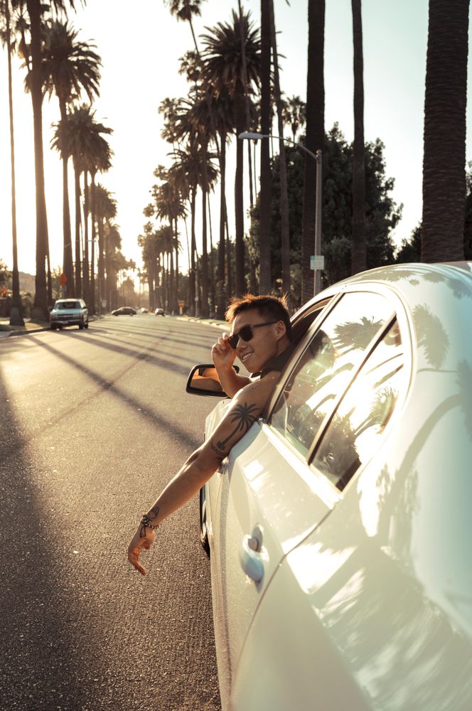 Man sneaking his head car window near palm trees during sunset