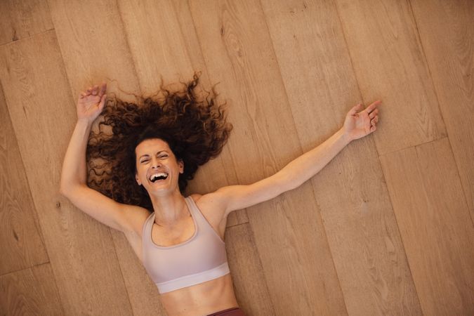 Top view of a woman lying on hardwood floor and laughing after exercising