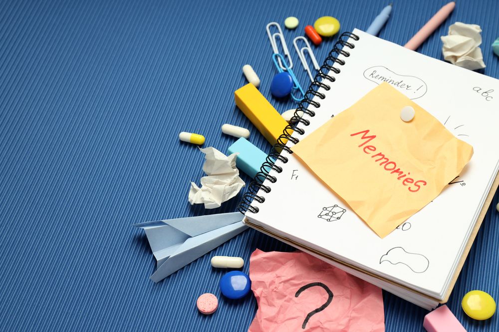 “Memories” post it note on book with pills, paper clips and pens on blue background, copy space