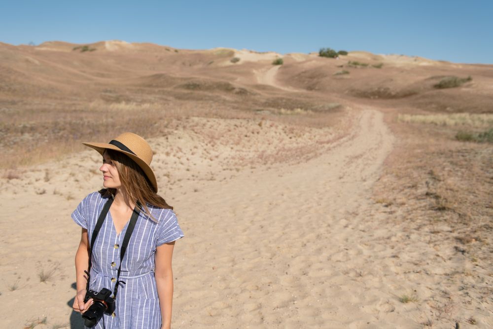 adult woman in straw hat and dress with camera walking on country path