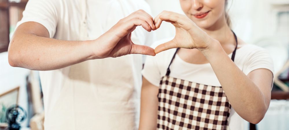 Man and woman standing in the kitchen at home making heart shape with hands