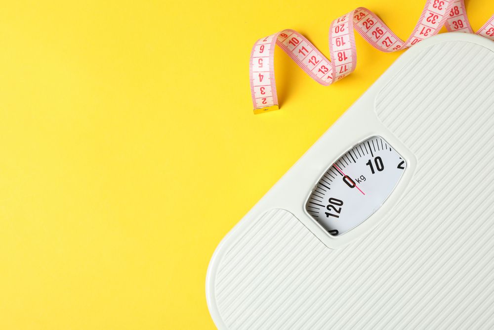Scales and measuring tape on yellow background. Weight loss concept