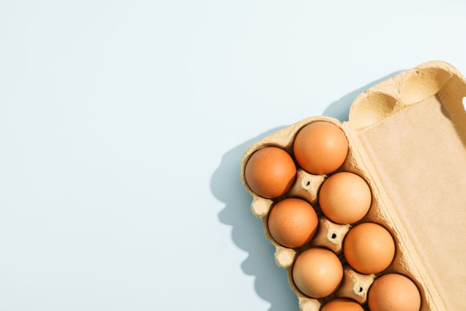Few raw chicken eggs in carton box on light background, space for text