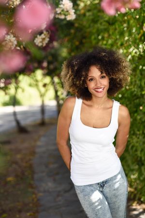 Young Black woman with afro hairstyle smiling in park, vertical