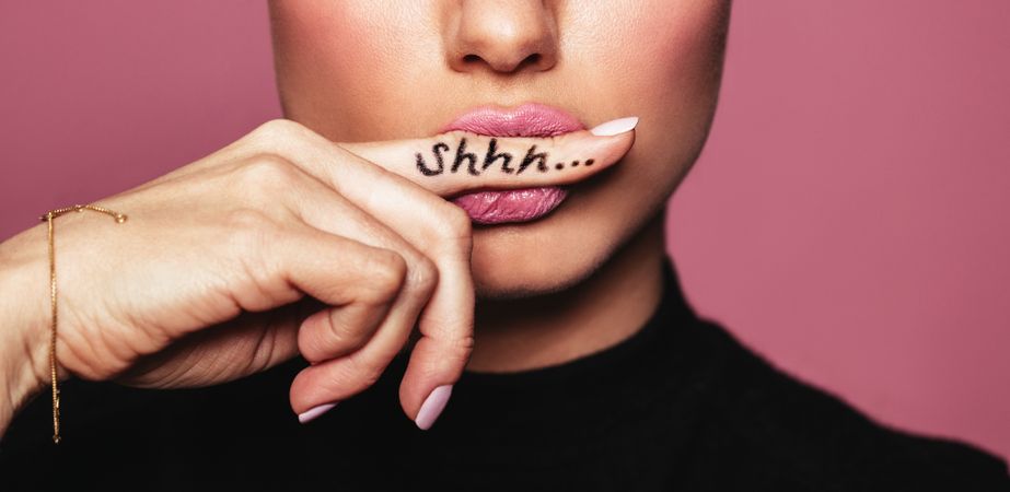 Cropped shot of young woman biting finger with shhh word