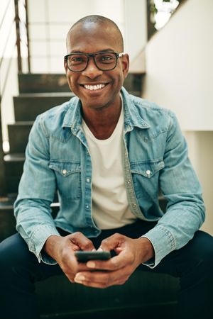 Portrait of smiling man in jean jacket and glasses with cellphone