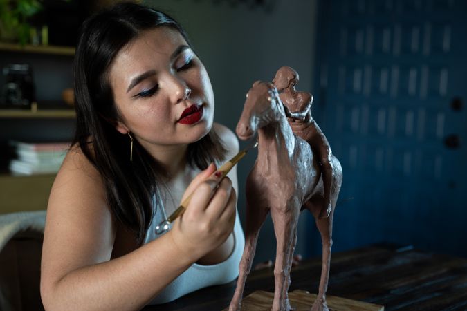 Young woman working on clay sculpture with clay tools
