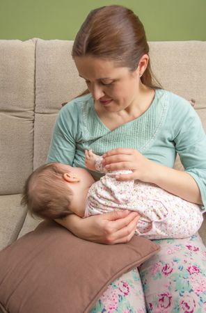 Baby breastfeeding with mother on couch, vertical