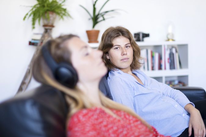 Woman looking at camera while friend sleeps on couch