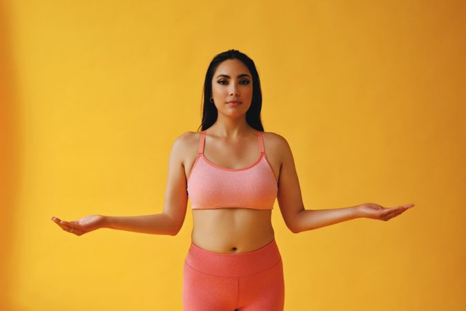 Hispanic female in yoga clothes with arms out in pose in yellow room, copy space