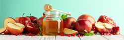 Fresh pomegranate, apples, pot of honey with dipper on mint background, wide orientation