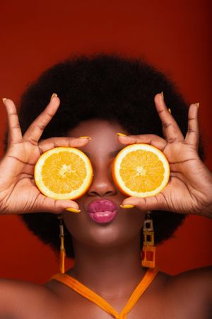 Woman with afro hair holding sliced oranges to her eyes