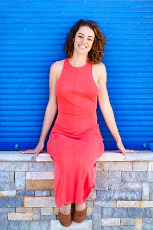 Content woman in summer dress leaning on brick wall in front of blue shutter