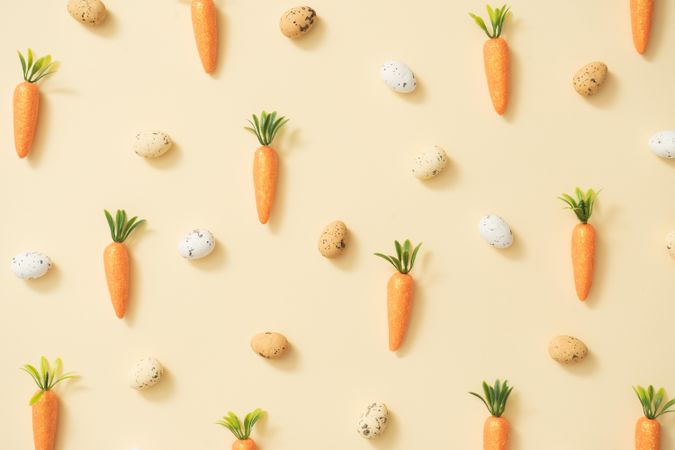 Easter eggs and carrots on pastel yellow background