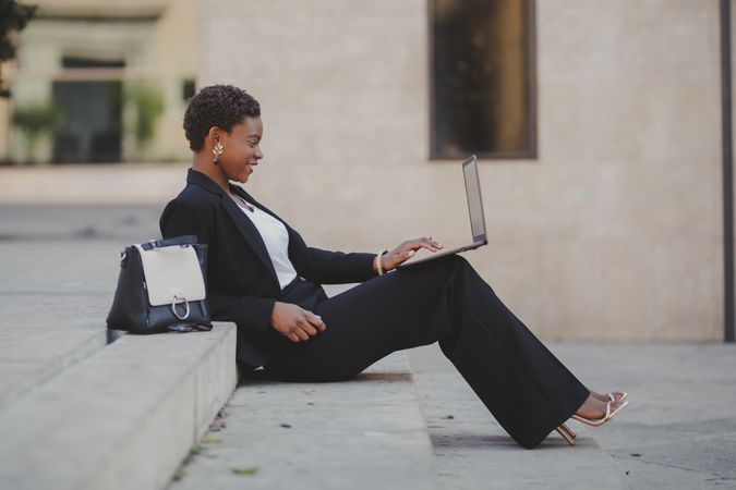Stylish Black woman with laptop on steps near handbag