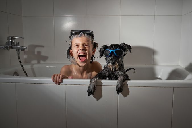 Cheerful boy with dog in bathtub