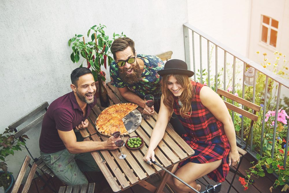 Friends with pizza, olives and red wine taking a picture of themselves on patio