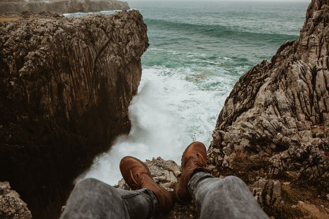 Person sitting on edge of cliff near water